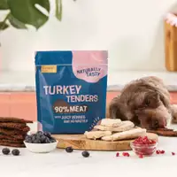 A dog eating a tender next to a apcket of Turkey Tenders