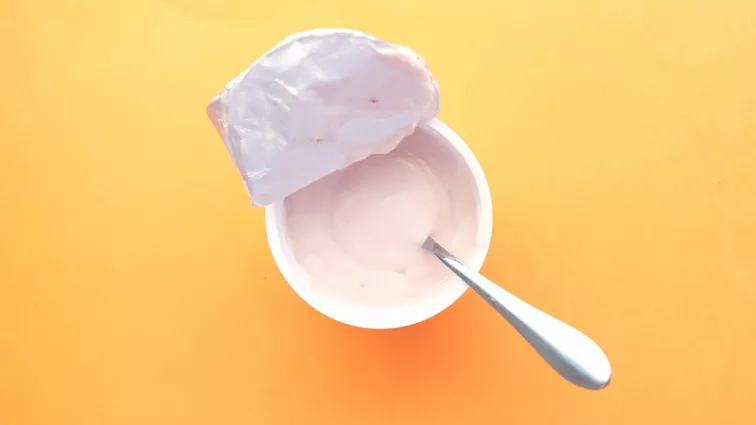 Kubeczek z jogurtem na żółtym tle.