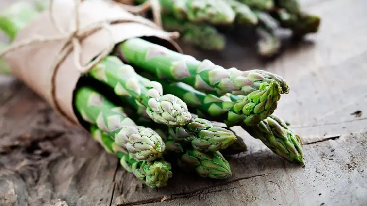 Pęczek świeżych zielonych szparagów owinięty papierem.