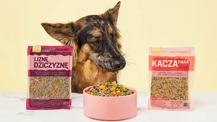 Pes sledující misku s jídlem mezi sáčky s porcemi Kachní s kuřecím a Zvěřinové hody.