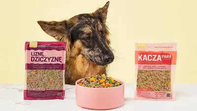 Pes sledující misku s jídlem mezi sáčky s porcemi Kachní s kuřecím a Zvěřinové hody.