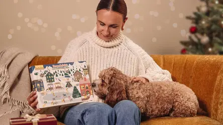 Kobieta siedząca na kanapie z psem i kalendarzem adwentowym PsiBufet.