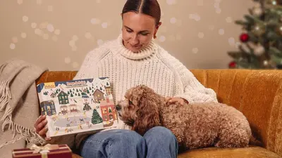 Kobieta siedząca na kanapie z psem i kalendarzem adwentowym PsiBufet.