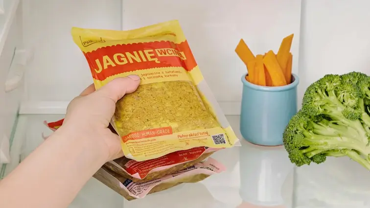 Ruka vyndávající z lednice kapsičku s čerstvým krmivem pro psa.