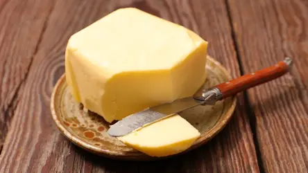 Kawałek masła na ceramicznym talerzyku z nożem do smarowania.
